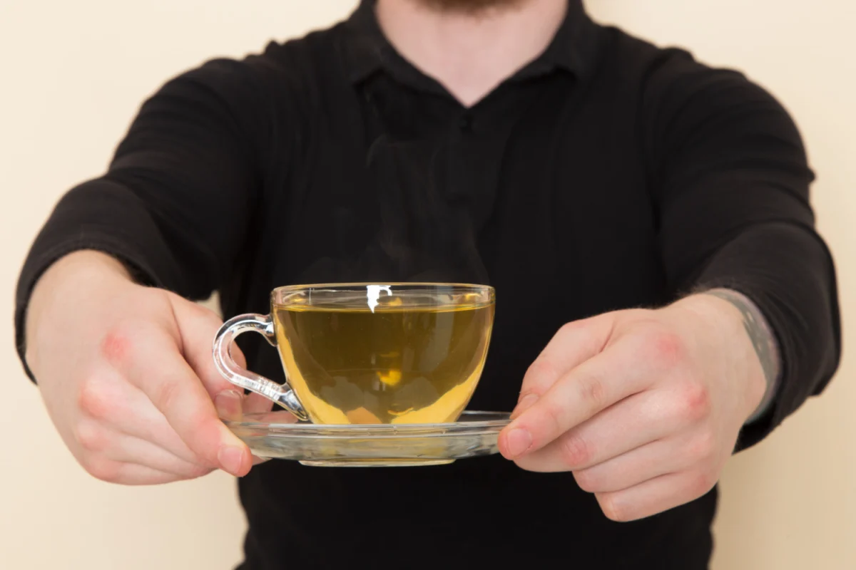 Man presenting a steaming cup of green tea, potentially part of a green tea shot recipe.