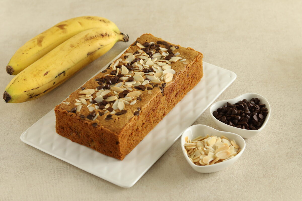 Freshly baked banana bread loaf with a golden crust, sprinkled with walnuts on top, resting on a wooden cutting board.