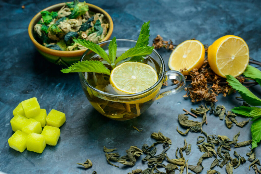 A cup of green tea surrounded by fresh tea leaves.