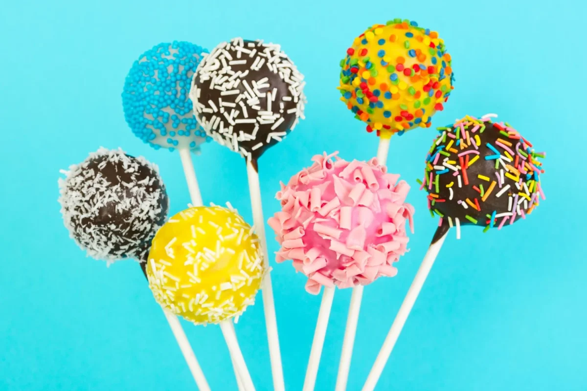 Assorted cake pops with colorful sprinkles against a vibrant blue backdrop.