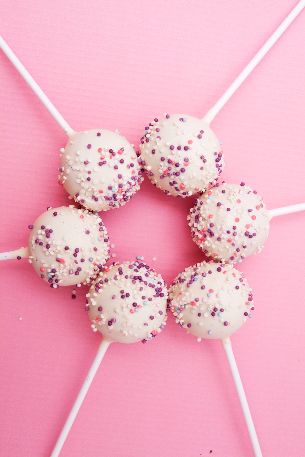 White chocolate cake pops with colorful sprinkles on a pink background.