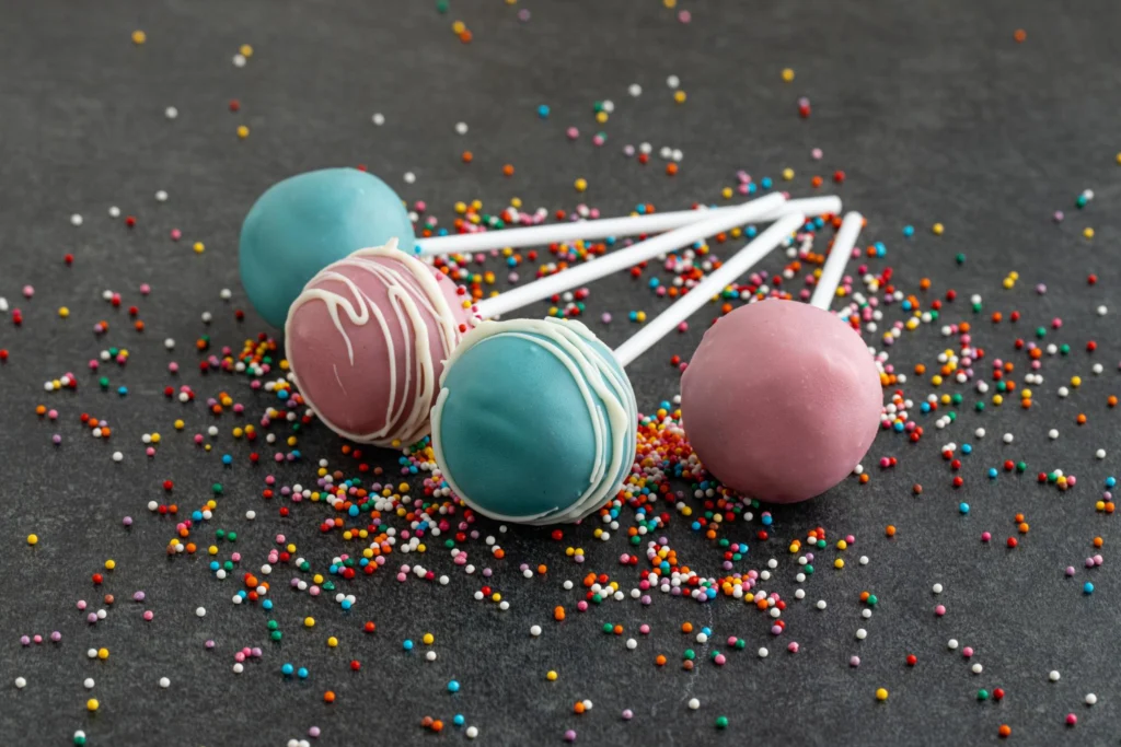 Assorted cake pops with a smooth chocolate coating, lying among colorful sprinkles.