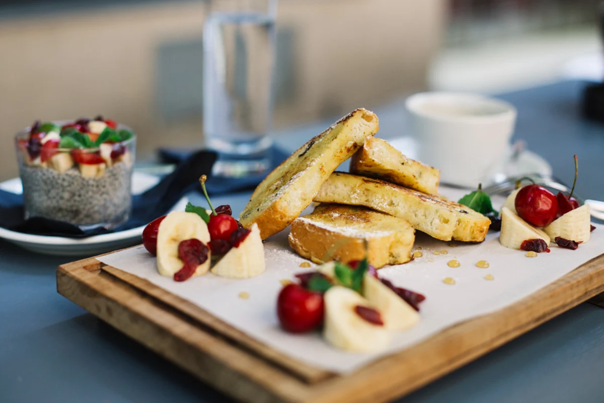 A delectable serving of French toast arranged on a wooden platter, accompanied by fresh cherries, banana slices, and a chia seed fruit cup, epitomizing the perfect use of French toast batter.