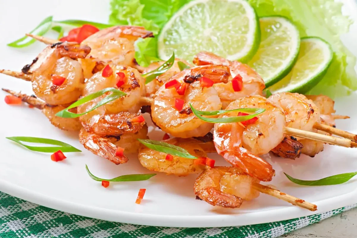 Grilled shrimp skewers garnished with spring onions and chili, served with lime wedges.