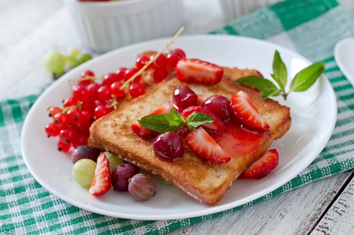 Savory French toast topped with fresh strawberries, red currants, and a mint leaf, showcasing a delicious example of French toast batter use.