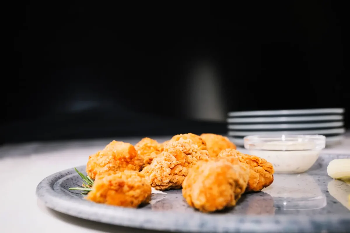 Crispy fried chicken pieces on a plate with dipping sauce, set against a dark backdrop.