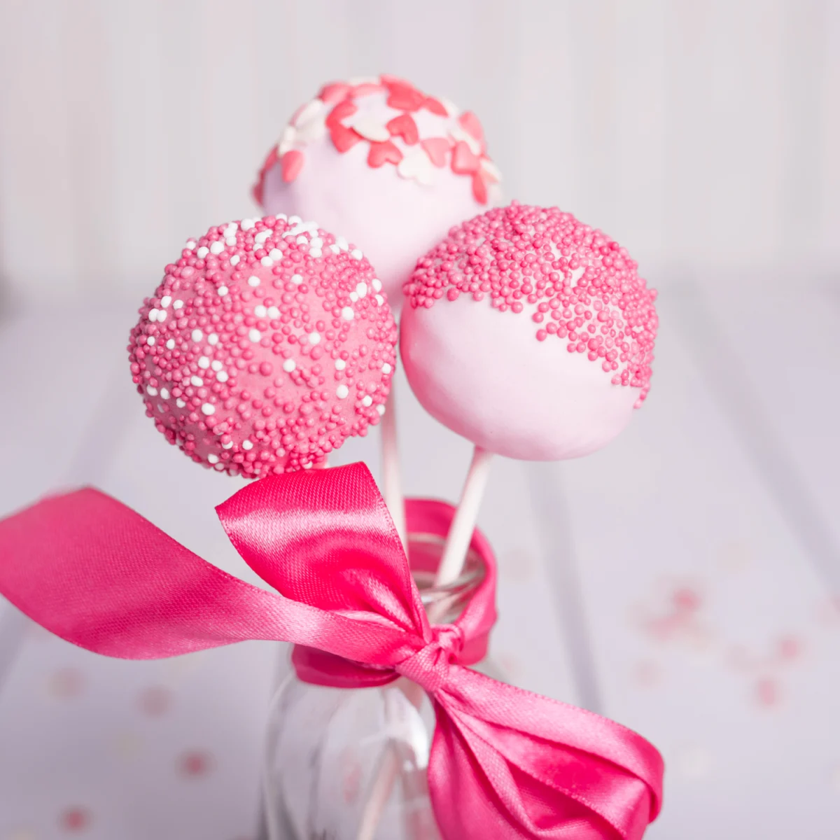 Elegant pink cake pops with sprinkles, tied with a satin ribbon.