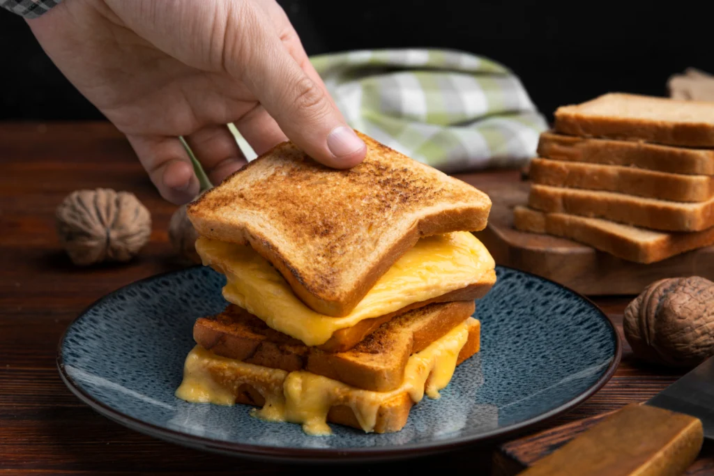 A stack of French toast with melting cheese on a blue ceramic plate, a hand placing the top slice