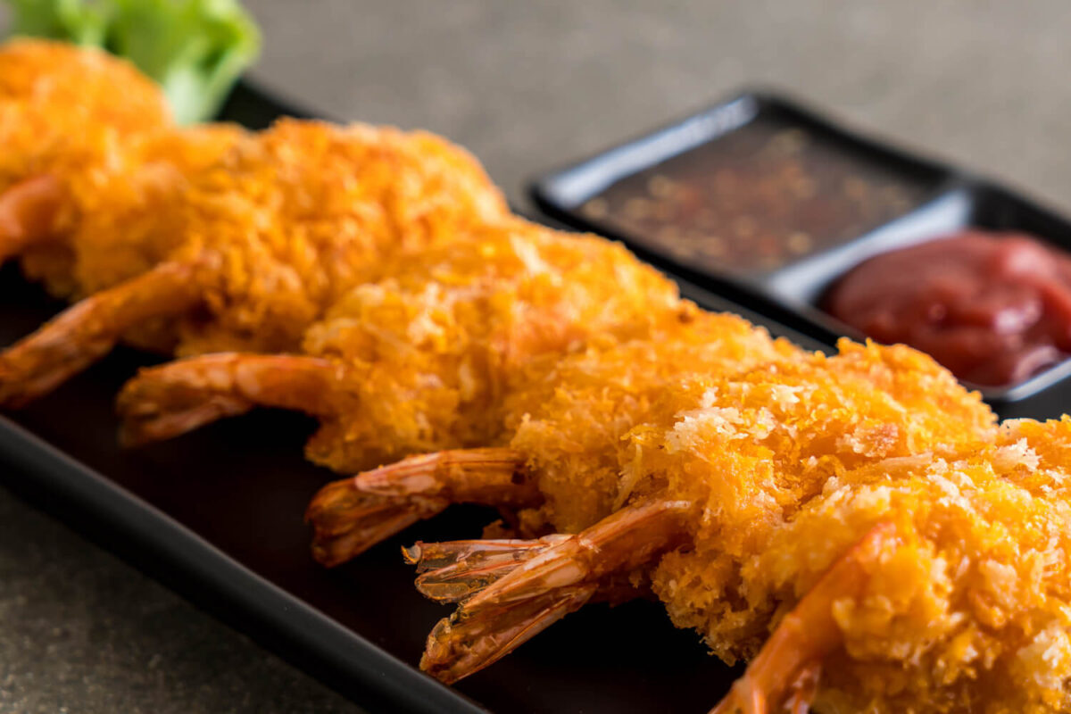 Crunchy golden-fried shrimp served with dipping sauces on a sleek black plate.