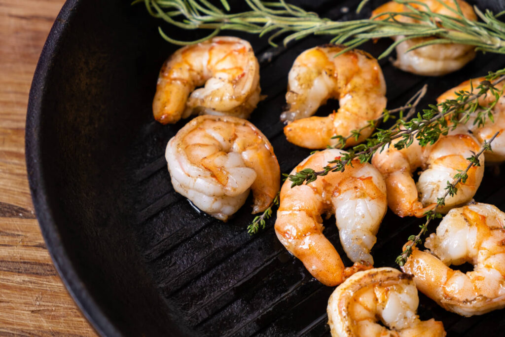 Grilled shrimp garnished with fresh thyme in a cast iron skillet.