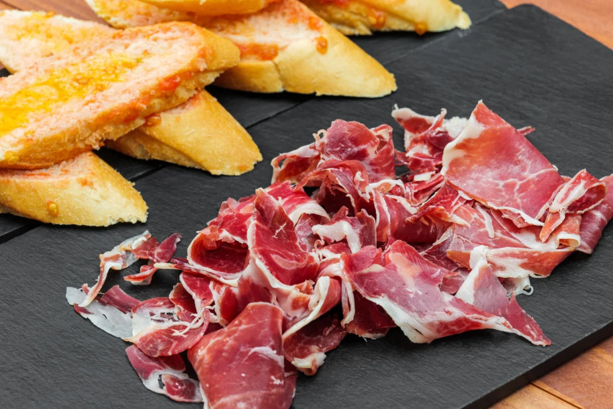 Thinly sliced Capicola alongside crispy, golden garlic bread on a slate board.