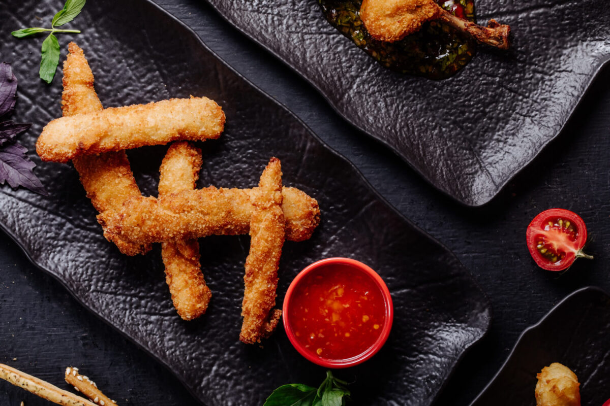 Crispy fried shrimp on a sleek black plate with dipping sauce and fresh herbs.