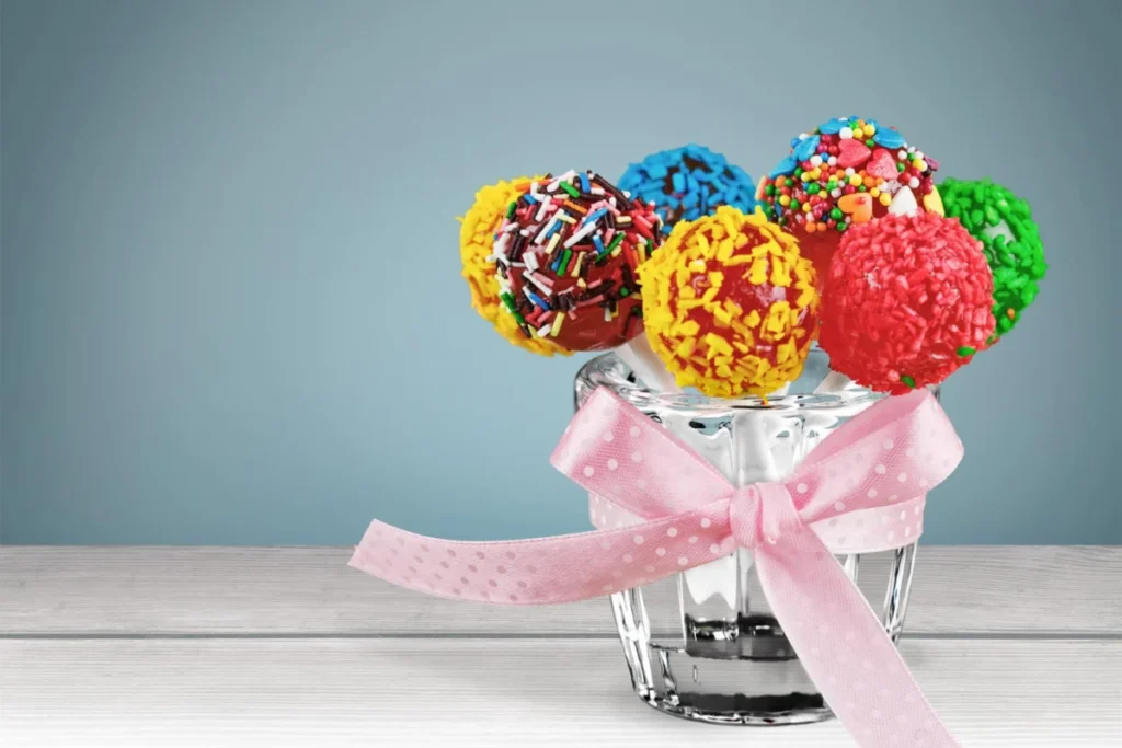 Vibrant cake pops with colorful sprinkles in a glass jar tied with a pink ribbon