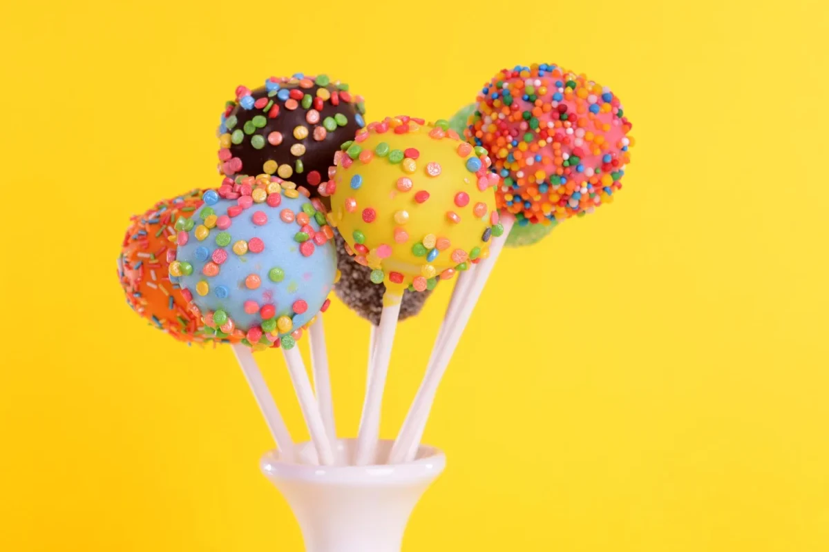 Assorted cake pops with colorful candy sprinkles against a bright yellow background