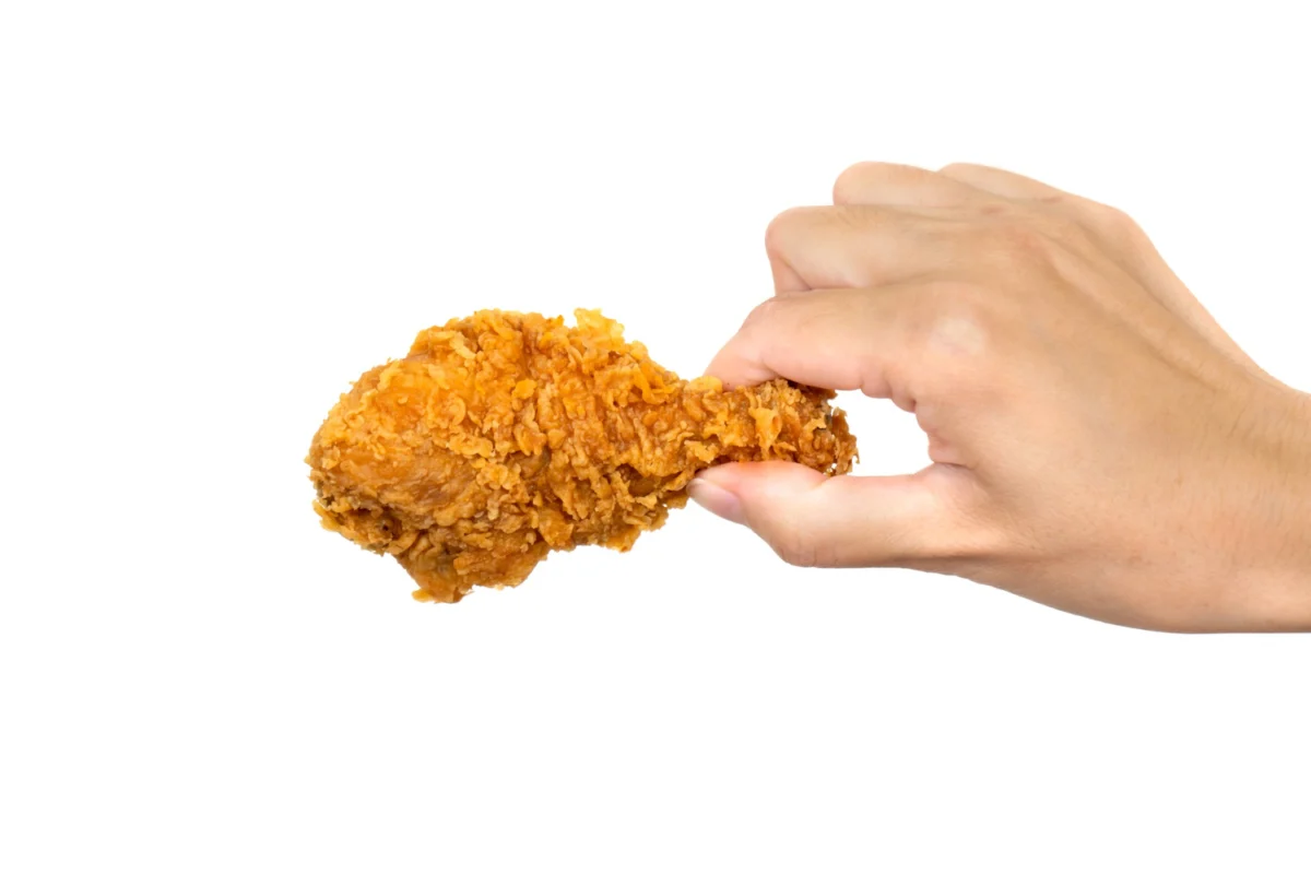 A hand holding a piece of crispy fried chicken isolated on a white background.