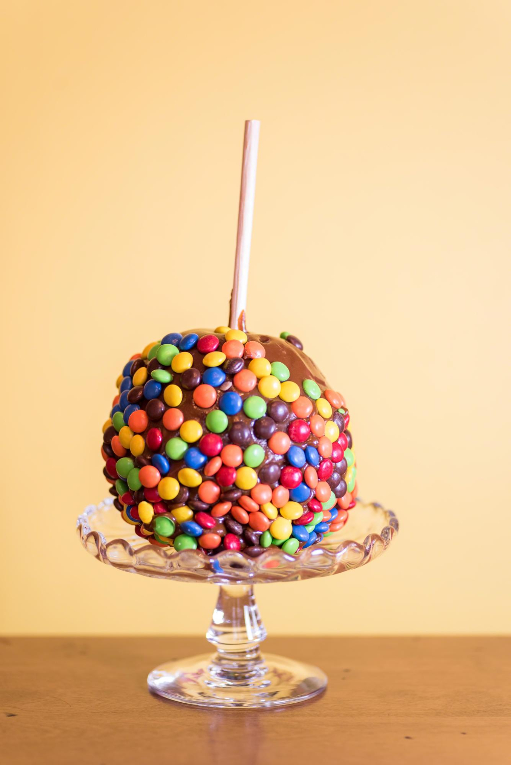 Chocolate apple covered with colorful candy pieces on a glass pedestal.