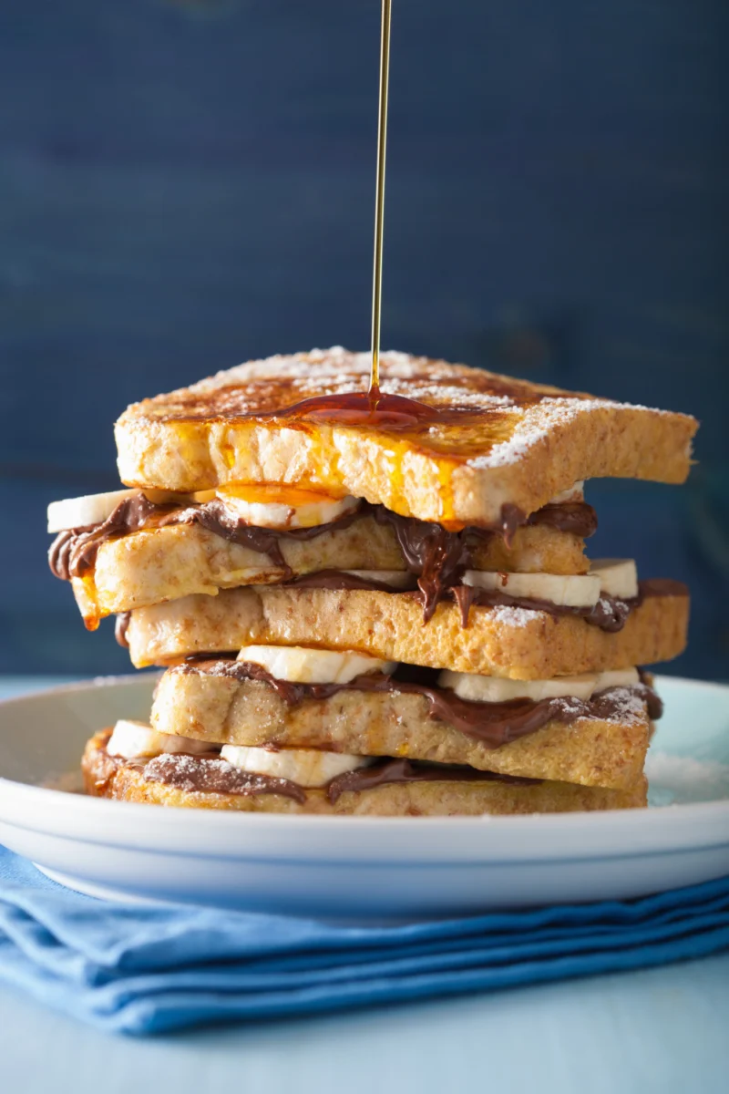 Stack of French toast with banana and chocolate spread, drizzled with syrup