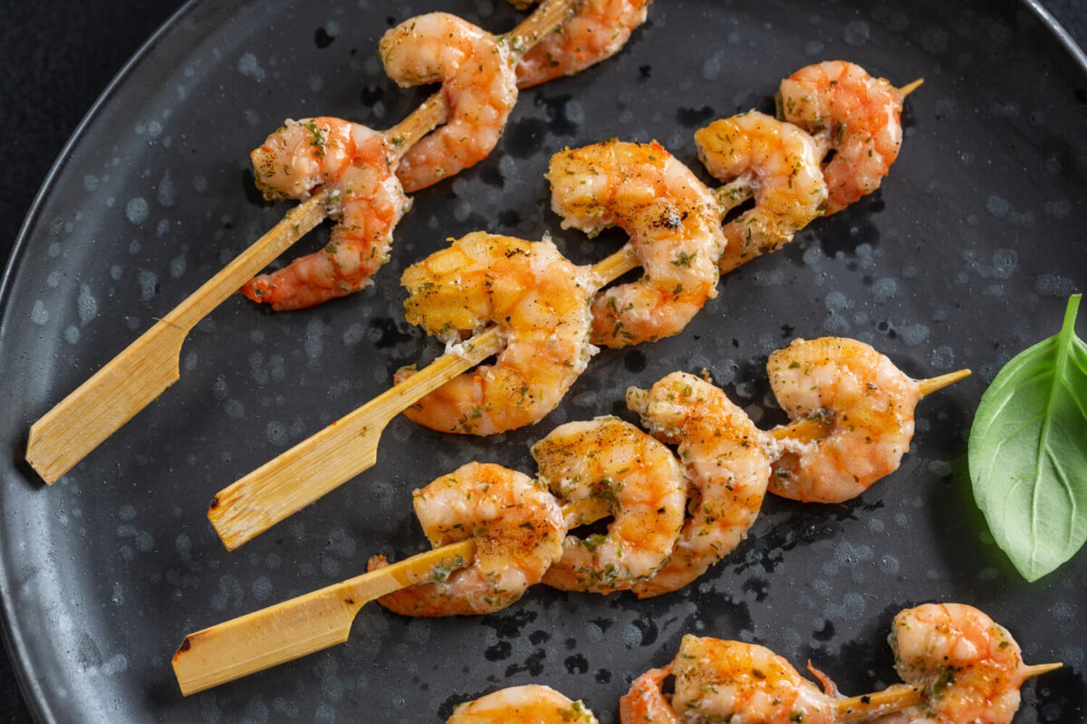 Skewered grilled shrimp seasoned with herbs on a modern black plate.