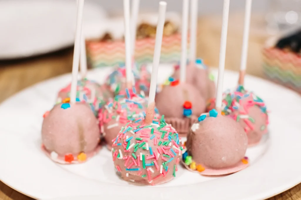 Colorful sprinkle-coated cake pops with a smooth, rounded appearance on a white plate, illustrating a guide on how to make perfect round cake pops.