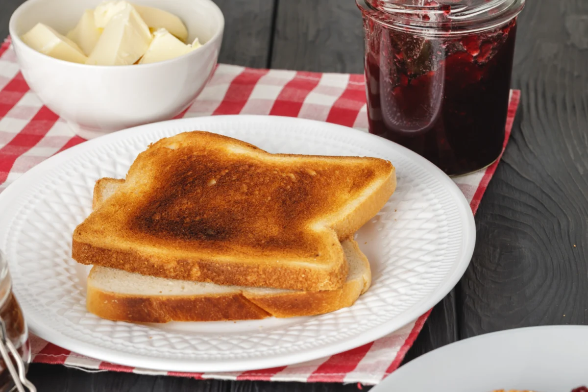 Golden-brown toasts on a white plate with butter and jam in the background, ready for a classic French toast preparation.