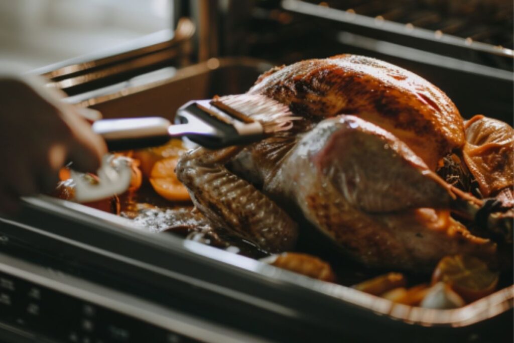 A close-up shot of a turkey being basted in an oven with a turkey baster.